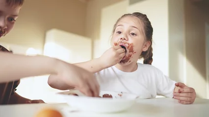 Muurstickers baby boy and girl eat chocolate. dirty little baby kids in the kitchen eating chocolate in the morning. happy family eating sweets kid dream concept. baby sweet dirty face eating chocolate cocoa © ibragimova