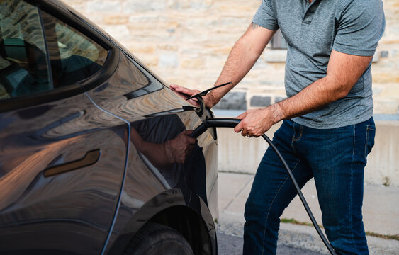 Close up of man plugging EV charger into electric vehicle outside.