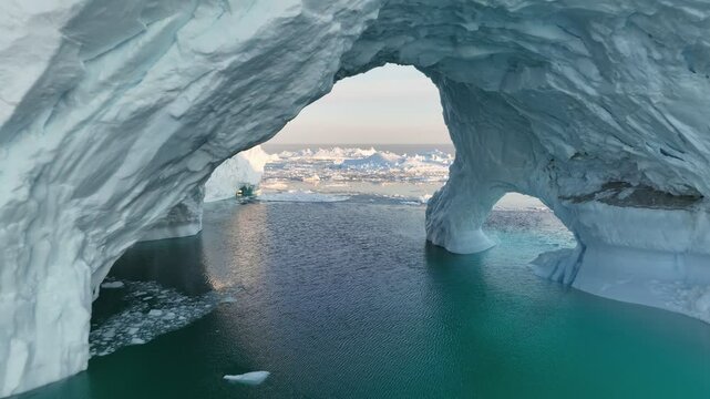 Icebergs from melting glacier float in Disco Bay, near Ilulissat, Greenland. Gaint iceberg with ice cave melting in the ocean. Aerial shot, climate change concept