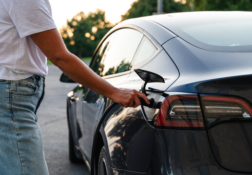 Close up of woman plugging EV charger into electric vehicle outside.