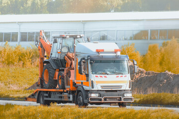 Tow truck moving excavator on highway through countryside on sunny summer day