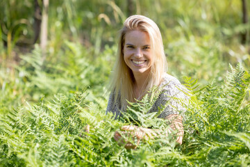 A beautiful woman enjoying the summer warmth: a smile among the greenery, embraced by ferns