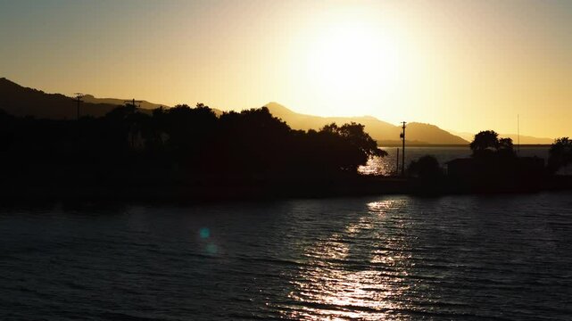 Arial view on sun coming trough the trees shiluette on a island in a lake watter Sunset, Drone, 4k, California