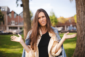 Perplexed and disappointment good-looking brunette long hair female student jeans jacket, shirt and top frowning shrugging with spread hands near shoulders saying what the hell walk in park.