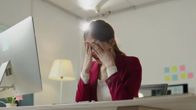 Businesswomanman is seriously stressed and upset working on tablet and document paperwork and headache due to office syndrome on laptop and paperwork in the office.