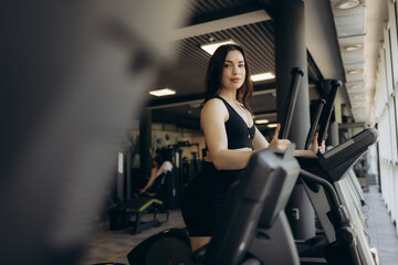 Beautiful young woman doing cardio on a stationary bike while smiling