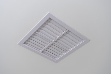A white plastic ventilation grille with small holes for ventilation, installed on the ceiling to remove air from a room.