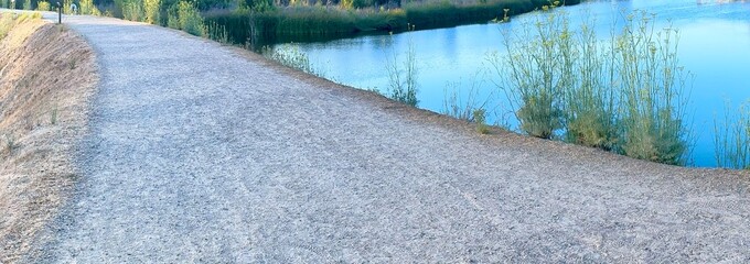 A gravel path runs alongside the serene waters of Calavera Lake in Carlsbad, California, with lush...