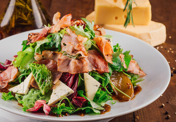 Delicious salad with jamon, pear and dor blue cheese on wooden table