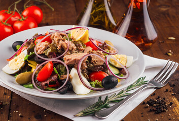 Fresh nicoise salad with tuna on a wooden table being prepared with eggs and tomatoes around