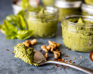 Basil Pesto on a spoon in front of glass jars