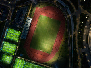 Aerial view of a well-lit sports complex at night with various fields bustling with activity in an...