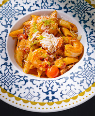 Penne pasta dish with shrimp and tomato sauce being sprinkled with grated cheese