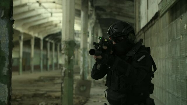 Portrait follow shot of a SWAT operator in black gear and an assault rifle with a green laser securing an abandoned warehouse