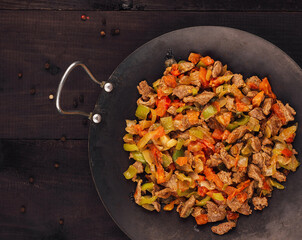 Wok containing sauteed vegetables and beef resting on wooden tabletop