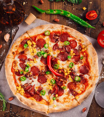 Delicious pizza with salami, corn and chili peppers lying on rustic kitchen table