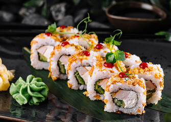 Crunchy tempura sushi rolls with chicken and cucumber lying on black plate