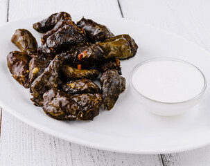 Serving plate presenting stuffed grape leaves dolma with yogurt dip on rustic white table