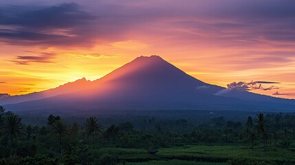 A dramatic sunset behind Mount Agung, casting deep shadows over the landscape and creating a striking silhouette of the volcanic peak.