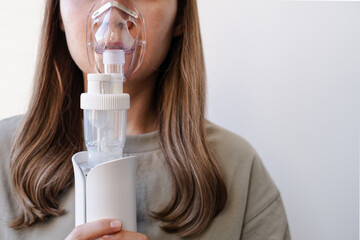 A girl breathes with the help of a nebulizer inhaler for the treatment of colds and coughs during...