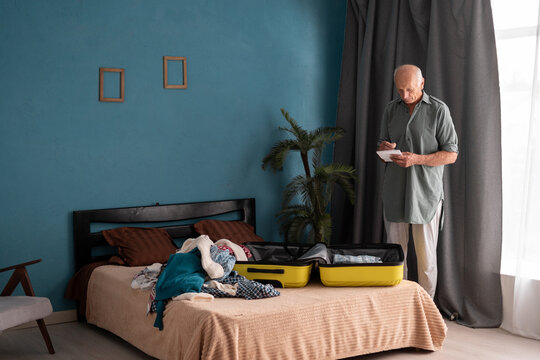 retired elderly man with checklist packing suitcase for weekend trip