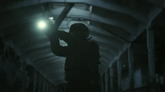 Special forces operator in stealthy black gear drawing his glock17 handgun from the holster and aiming with the flashlight turned on in a dark abandoned warehouse
