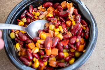 beans,corn,peas and carrots in black plastic bowl on brown background