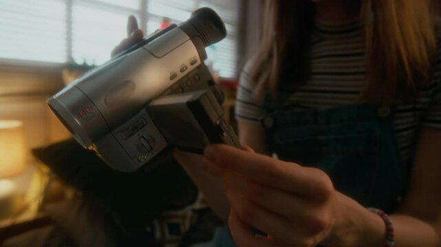 Tilt slowmo closeup shot of smiling gen Y girl using old retro video camera at home, outdated technologies, atmosphere of 1990s