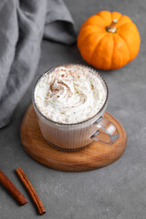 Spice latte with whipped cream in glass cup on wooden board on dark  background with decorative pumpkin and cinnamon stick.