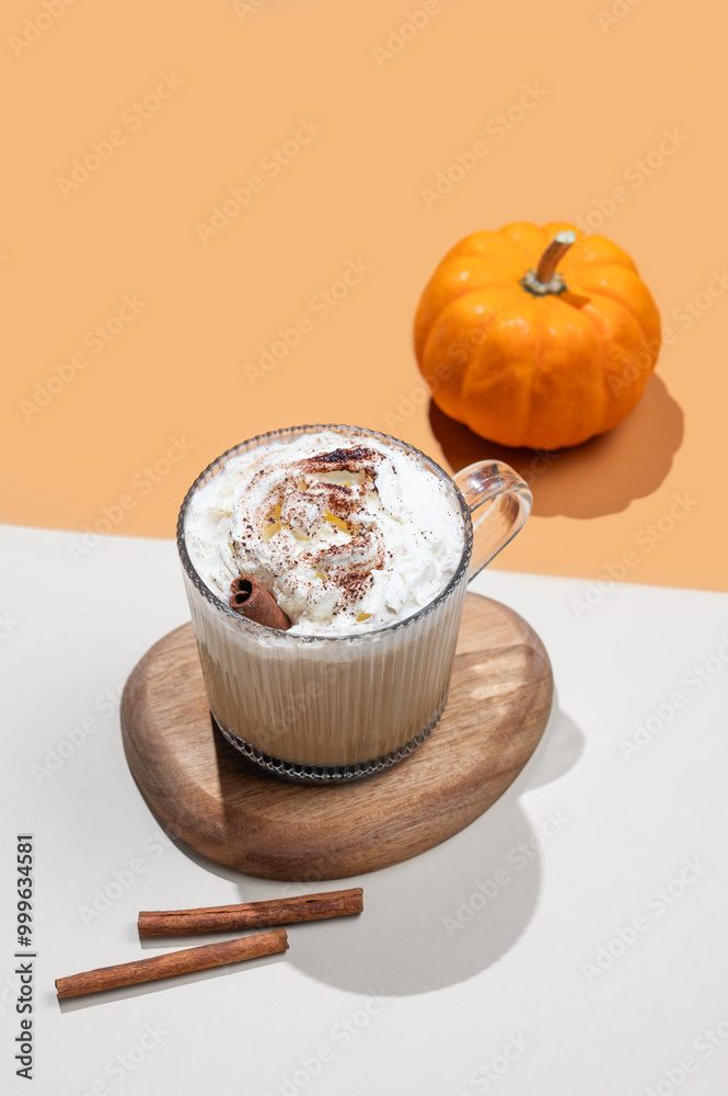 Wall mural Spiced pumpkin latte in glass cup on orange background with decorative pumpkins and cinnamon sticks.