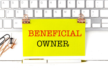 Business concept with beneficial owner message on yellow paper, keyboard, and office supplies on desk