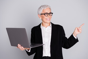 Portrait of charming successful senior lady wear black stylish suit demonstrate promo empty space isolated on grey color background