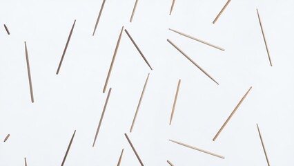 Multiple wooden sticks are lying on a white background, forming a seemingly random pattern with their tips pointing in various directions