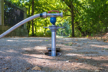 close-up of a metal water valve or hydrant, connected to a hose, set in a park or outdoor area