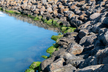 A rocky shoreline in Portarlington, Bellarine Peninsula of Victoria, Australia, with large boulders lining the water’s edge as part of a breakwater or sea wall to protect infrastructure from erosion.
