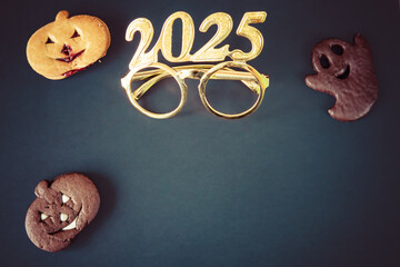 Various Halloween ghost sugared gingerbread cookies, chocolate butter pumpkins and shiny glasses year 2025. on black background. Top view copy space for text