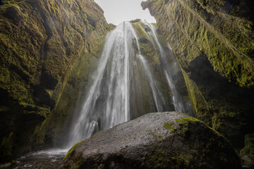 Gljufrabui waterfall tumbles before a great boulder in a narrow mossy canyon, Icleand