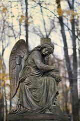 stone statue of sad angel on old cemetery, autumn nature background. Design for condolence, mourning card or obituary. symbol of religion, faith, mourn, memory. all saints day, All Souls Day