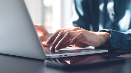 Closeup, woman typing on laptop computer on office table, backlit, internet technology, online working, remote job, smart device