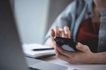 Business woman using mobile phone with laptop computer on table. Woman surfing the internet, searching the information on smartphone during working on laptop computer at home office, online job