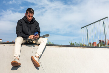 copyspace Relaxed skater texting on smartphone while sitting at half-pipe edge during break