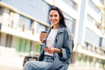 Photo of cheerful pretty lady dressed grey jacket reading modern device enjoying coffee outdoors...