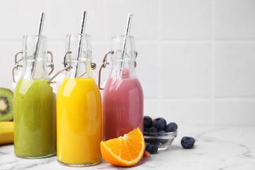 Glass bottles of tasty smoothies and different products on white marble table, space for text