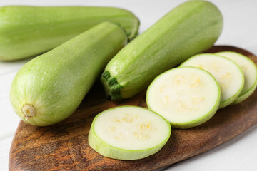Board with fresh zucchinis on white table, closeup