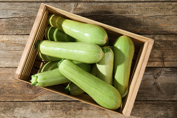 Crate with fresh zucchinis on wooden table, top view