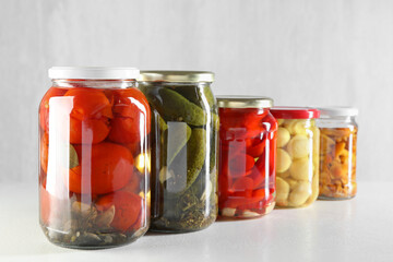 Tasty pickled vegetables and mushrooms in jars on white background, closeup