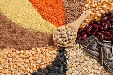 Different types of cereals, legumes and seeds with spoon on table, closeup