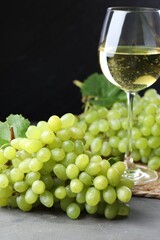 Fresh ripe grapes and glass of wine on grey table