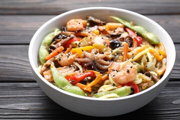 Stir-fry noodles with sea food in bowl on wooden table, closeup