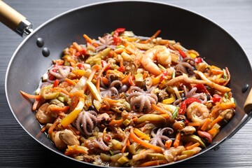 Stir-fry sea food in wok on black wooden table, closeup